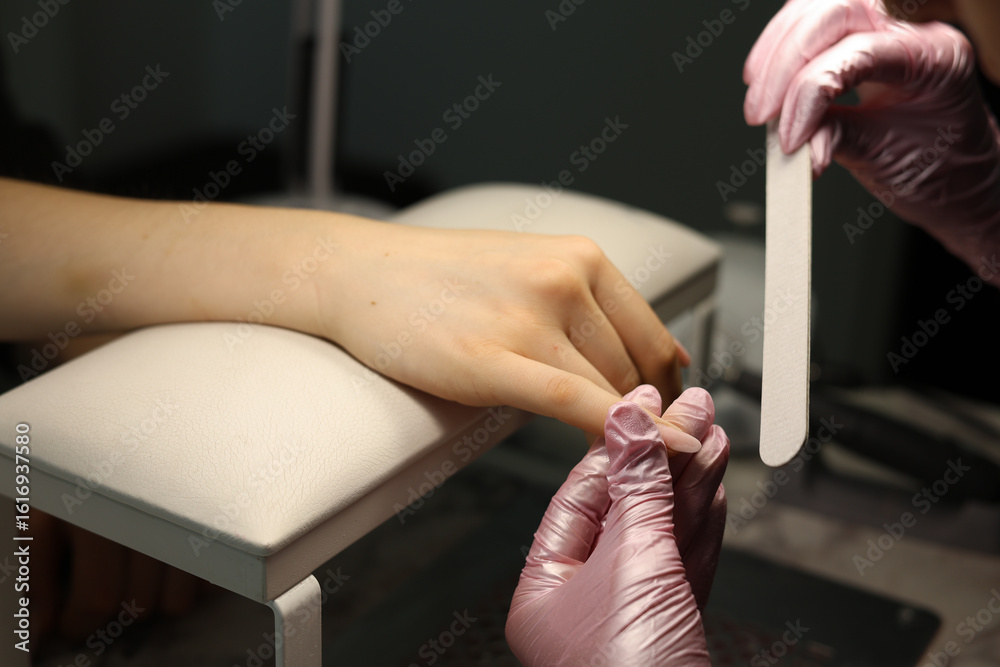 Obraz premium A skilled manicurist in black gloves files and shapes a client's nails, focusing on precision and care during a manicure session