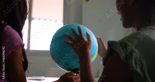 Young children engaging in a science or geography learning activity, exploring a globe indoors with natural light streaming through a window 