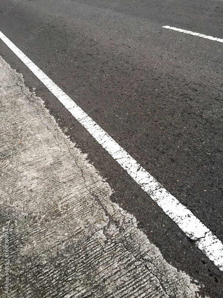 Obraz premium A straight, unbroken white line next to the edge of a paved road as a boundary between vehicles and pedestrian areas
