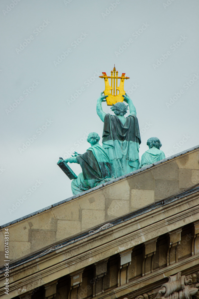 Fototapeta premium Gilded Statue atop Historic Parisian Building Under Overcast Sky. The statues appear to be made of a weathered, green-patina bronze