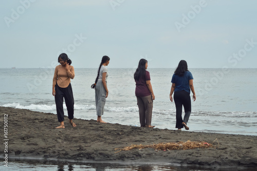The girls pause to watch the movement of the waves while standing on the sand between brackish water and the sea, absorbed in the tranquil morning view.