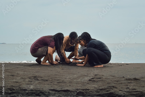 Obraz na plátně The girls huddle over wet sand as the tide laps nearby, sculpting shapes together while one remains soaked from earlier sea play