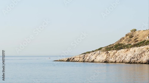 Wallpaper Mural Serene seascape with rocky shoreline and calm blue water under a vast sky in Varkiza, Greece. A distant boat leaves a gentle trail.  Torontodigital.ca