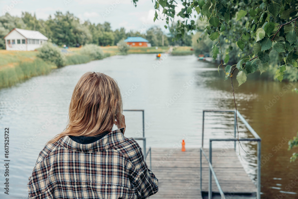 Fototapeta premium woman on dock by lake making phone call, surrounded by trees and water, concept of remote connection, slow living, mindfulness