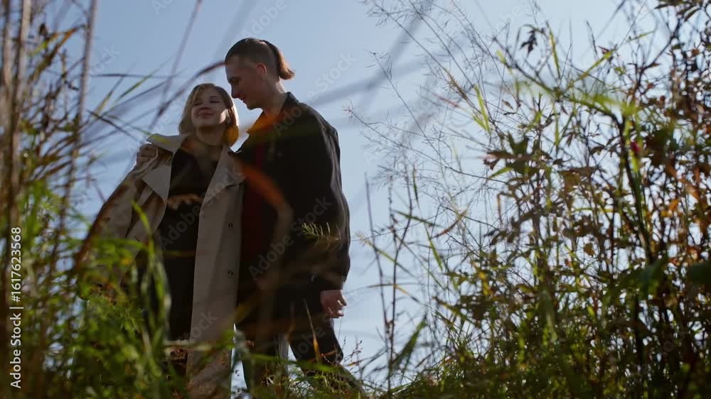 Stylish young couple sharing intimate moments, gracefully dancing and walking through golden autumn field, surrounded by tall grass under bright blue sky Stylish young couple sharing intimate moments, gracefully dancing and walking through golden autumn field, surrounded by tall grass under bright blue sky