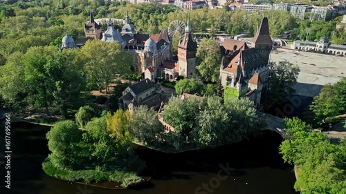 Morning aerial drone video zoom out to frame Vajdahunyad Castle, the artificial lake, and lush greenery of Budapest’s City Park all in one wide scenic shot.  