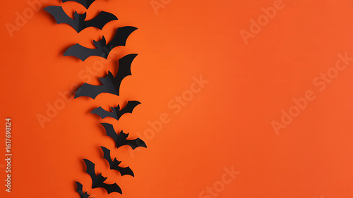 Black paper bats flying in a line against an orange background