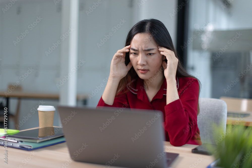 feeling stressed asian businesswoman working on laptop sitting at desk in modern office space for work online. feeling stressed asian businesswoman working on laptop sitting at desk in modern office space for work online.