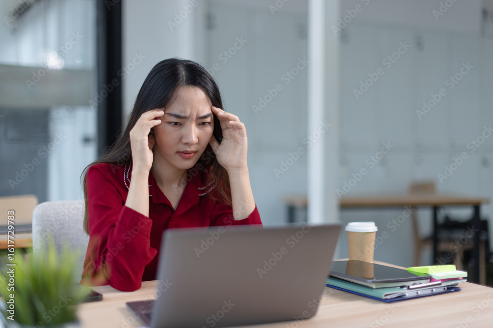 feeling stressed asian businesswoman working on laptop sitting at desk in modern office space for work online. feeling stressed asian businesswoman working on laptop sitting at desk in modern office space for work online.