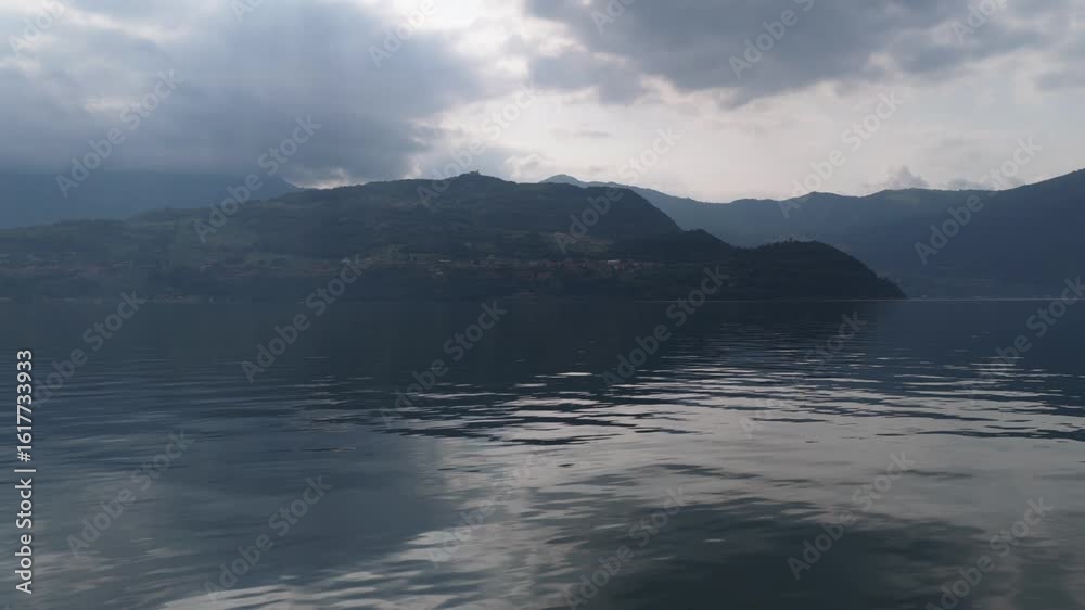 Dramatic aerial view of Lake Iseo with dark clouds casting shadows over the calm water and green hillside Dramatic aerial view of Lake Iseo with dark clouds casting shadows over the calm water and green hillside