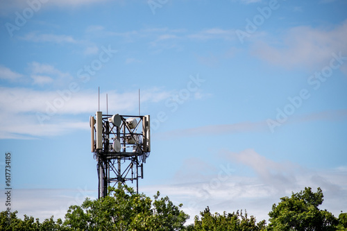 A mobile communication tower surrounded by green treetops under a bright blue sky. Modern technology and connectivity.