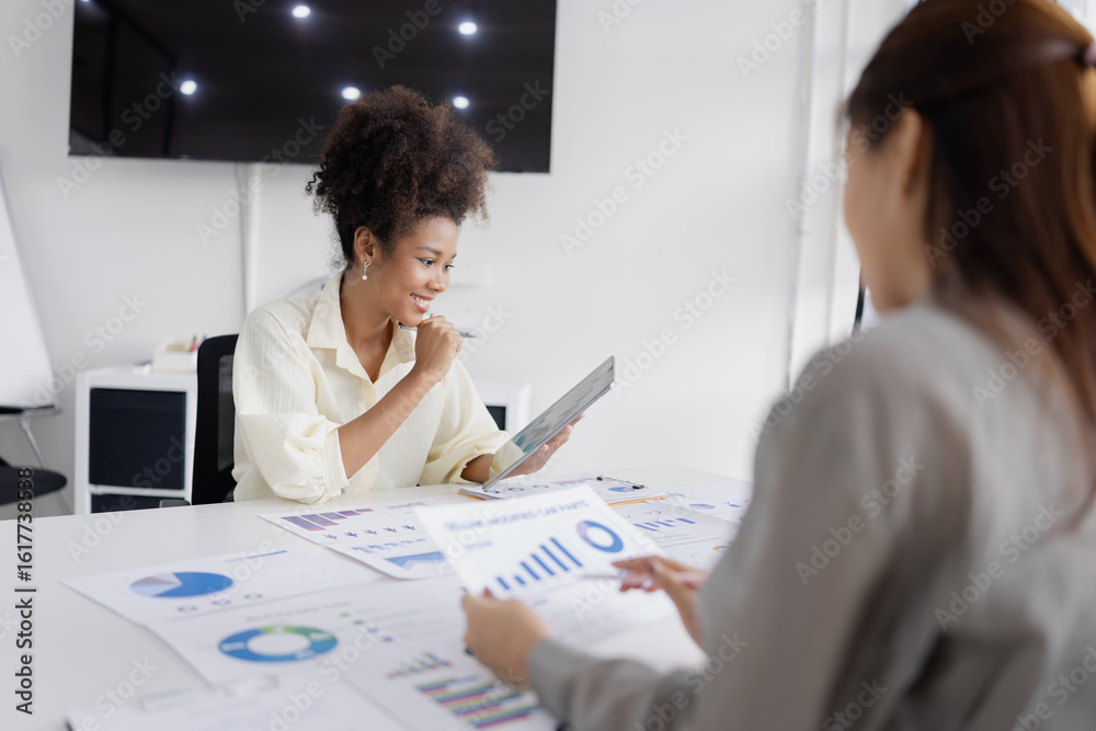 Fototapeta premium two businesswomen with analyzing financial documents working together in office, African American businesswoman and Asian businesswoman.