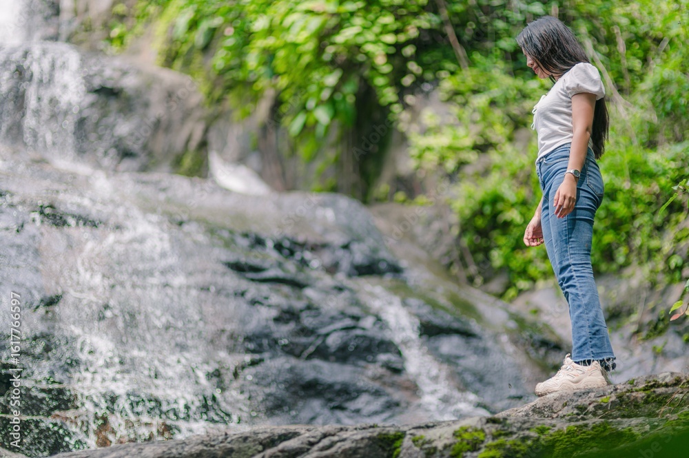 Obraz premium Woman Standing at the Base of a Serene Waterfall in Nature Scene