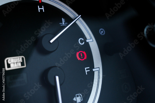 Red brake system warning light on car dashboard next to fuel and temperature gauge indicators.