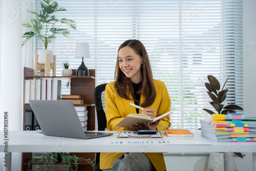 Foto Focused Professional in Office: An accomplished woman, immersed in her work, diligently takes notes at her desk, utilizing a modern laptop to enhance her professional efficiency