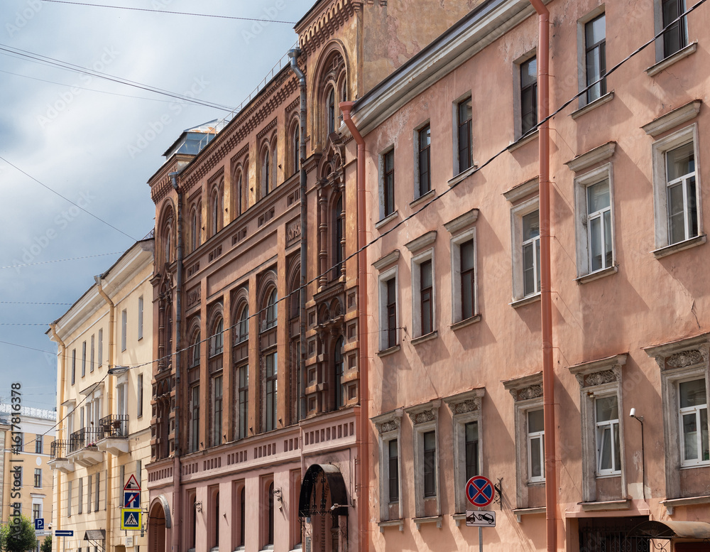 Fototapeta premium A row of orange, brown and white historic residential buildings with ornate facades and arched windows in city under a cloudy sky