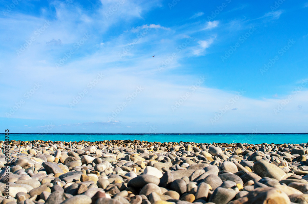 Pebble beach with blue sea, clear sky and airplane flying overhead Pebble beach with blue sea, clear sky and airplane flying overhead