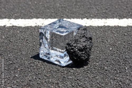 Clear cube, dark chunk on asphalt