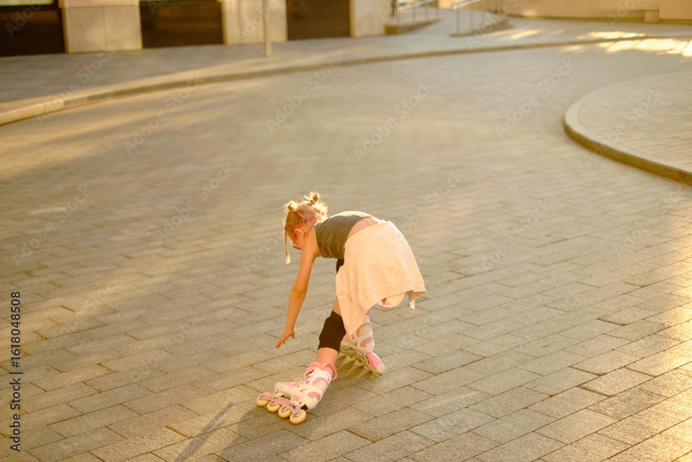 Obraz premium Young girl in pink glasses roller skating outdoors during sunset, wearing casual black top and beige skirt tied around waist, capturing playful childhood fun and lively urban atmosphere