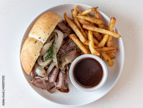 Delicious roast beef sandwich with french fries and au jus on white plate