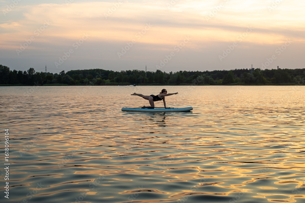 Naklejka premium woman doing yoga on sup board at sunset. outdoor summer activity. Sup yoga. Social Distancing. copy space. Mental Health