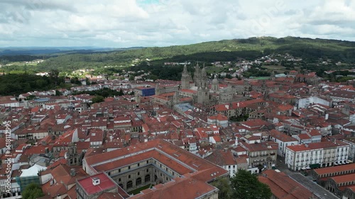 Aerial view of the cityscape with red rooftops and the Cathedral of Santiago de Compostela, set against lush green hills, Santiago de Compostela, A Coruña, Spain.