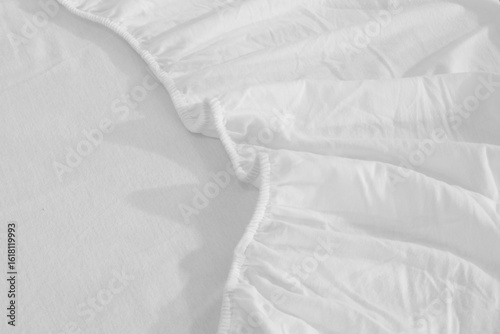 White cotton fitted sheet with elastic band bed corner, Bed corner on the bed close up photo, Fitted sheet or bed cover, Bed skirt closeup photo