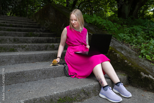 Fotografie Young woman works on her laptop in a summer park, her pet agama lizard lounging