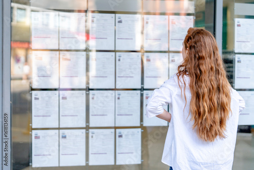 Young woman examines job listings posted outside a building in a busy urban area during the day