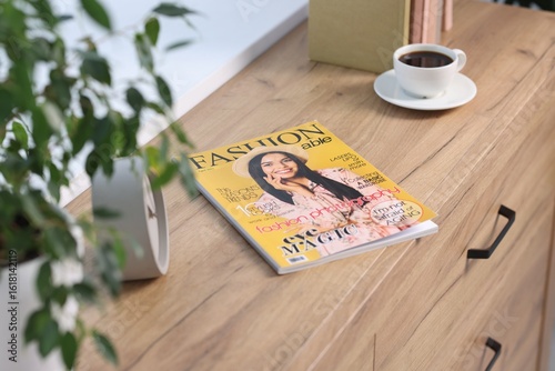Fashion magazine and cup of coffee on wooden table indoors