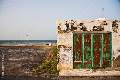 Weathered coastal structure with peeling paint and industrial setting in background, highlighting decay, shoreline infrastructure and urban periphery transformation.