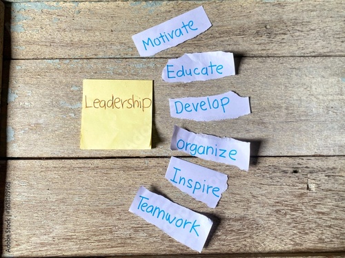 Adhesive note with Leadership written on it is surrounded by torn papers with various leadership qualities like Motivate, Educate, Develop, Organize, Inspire, and Teamwork.