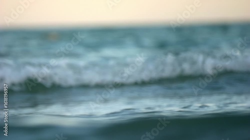 Telephoto shot of choppy sea at sunset with soft golden light and slow motion movement of waves.