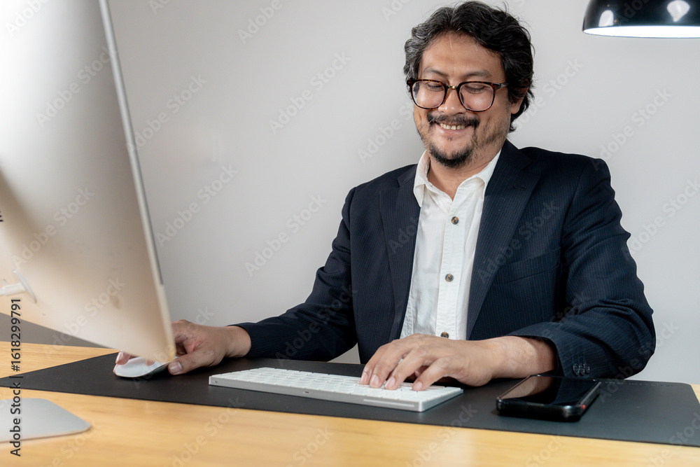 Fototapeta premium A cheerful male office employee working at his desk in a modern office environment, representing productivity and job satisfaction.