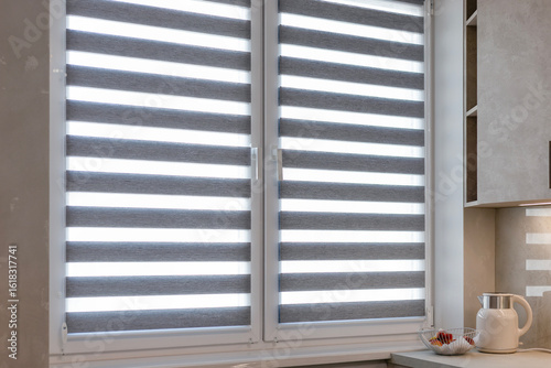 Double roller blinds closeup on the window in the kitchen interior. Dual roller shades in gray color. Zebra blinds. Duo system day and night for light control and modern window treatment.