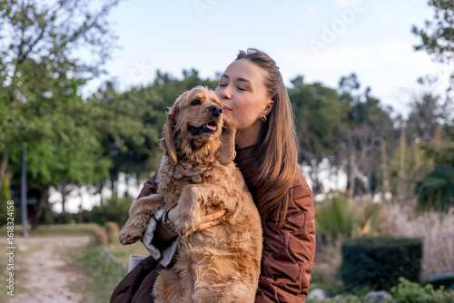 Fotografie A young Caucasian woman with long brown hair kisses a golden cocker spaniel