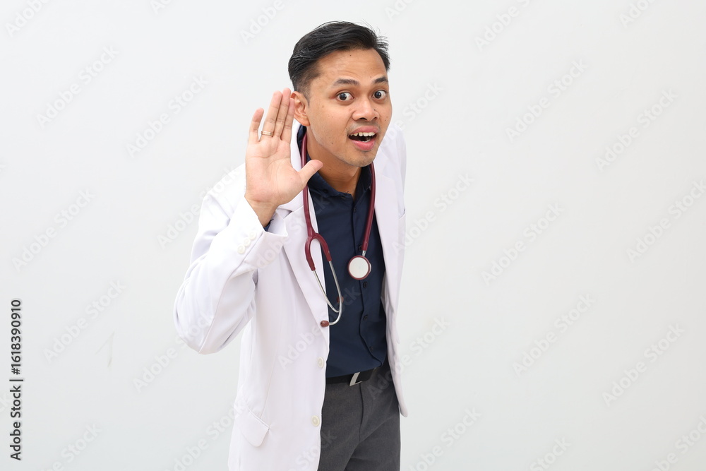Male doctor wearing doctor's coat and stethoscope standing, hand next to ear gesture listening to something Male doctor wearing doctor's coat and stethoscope standing, hand next to ear gesture listening to something