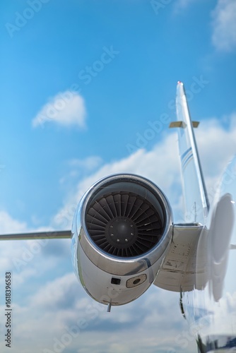 Jet engine captured with a long focal length, isolating the turbine detail while creating a blurred blue sky backdrop. The engine’s polished nacelle reflects light, highlighting precision engineering.