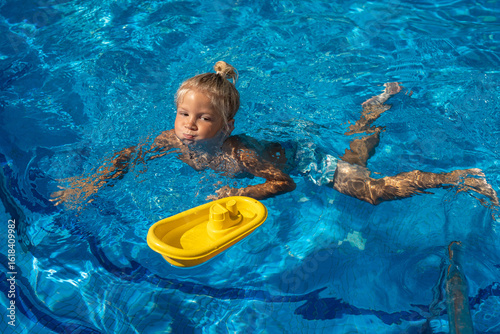 Fotografija Little blond boy swimming underwater in a bright blue pool, holding his breath w