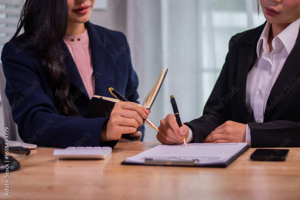 Obraz premium Female executives and female lawyers shake hands at a table in a courtroom to conclude a contract, providing legal advice, teamwork, and professional cooperation.