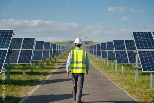 employee walking at a solar power farm, wearing safety vest and helmet . solar panel installation