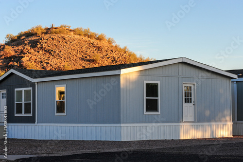 A manufactured home with vinyl siding and skirting is installed on a prepared lot, representing modular housing in a residential development setting