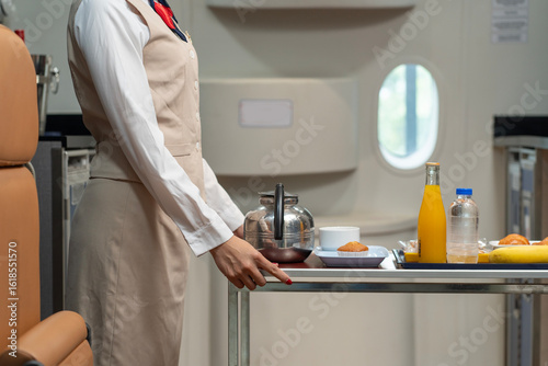 Asian flight attendants in uniform pushing a cart with food and beverages, tea, coffee, orange juice to serve passengers in the cabin during flight on the plane. Airline service concept.
