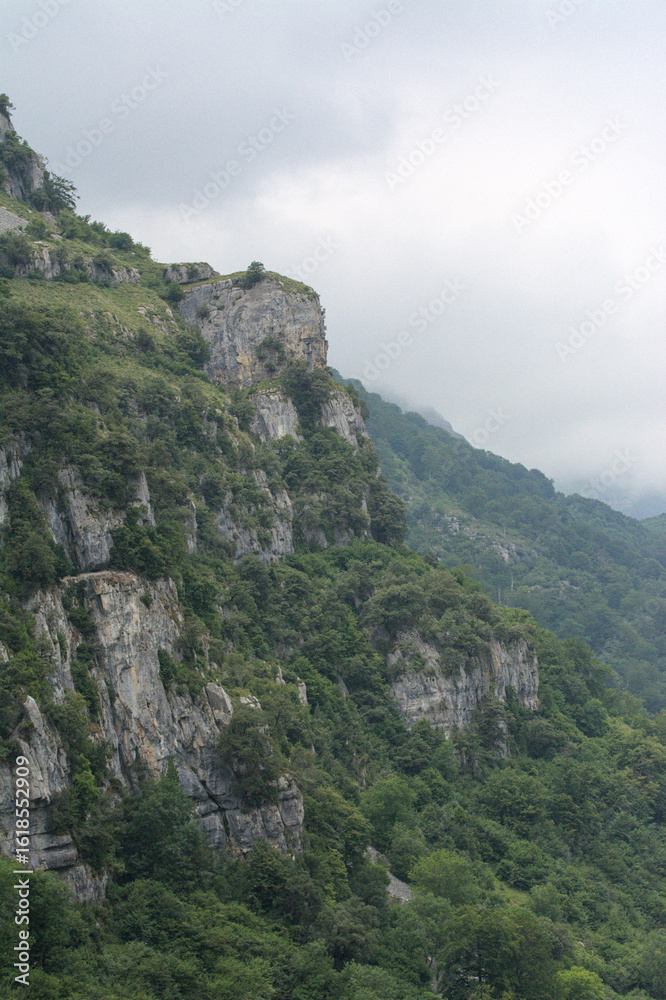 Naklejka premium Rugged mountain peaks meet winding road in Asón, Cantabria - Breathtaking Cantabrian valley with lush green forests, rugged mountains, and serene atmosphere, set amidst a natural.