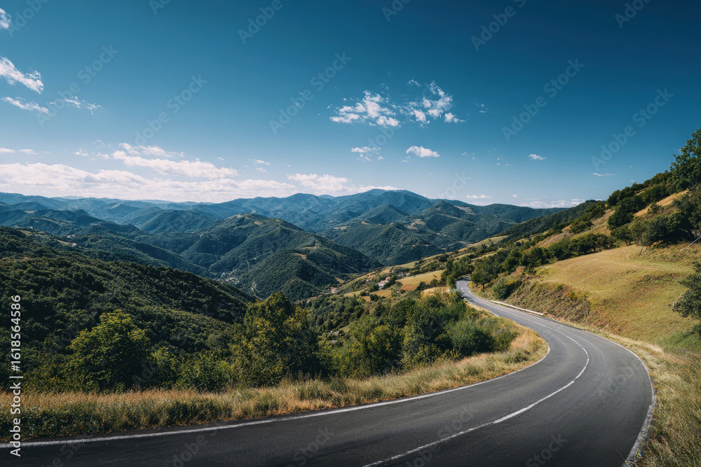 Fototapeta premium Winding mountain road through lush green hills under a vibrant blue sky on a sunny day