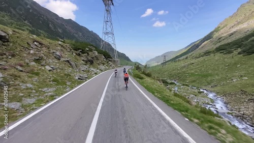 Three cyclists ride along a winding mountain road.  Stunning scenic view with lush green hills and a clear blue sky. Perfect for travel, adventure, or sports themes.