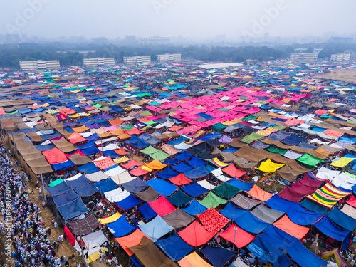 Aerial view of a sprawling tent city, a vibrant tapestry of colorful tarps, stretches out under a hazy sky, a temporary metropolis of faith and community, Dhaka, Dhaka Division, Bangladesh.