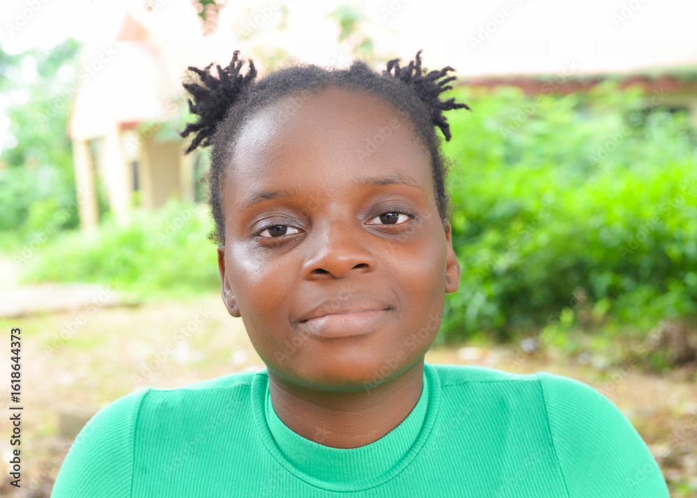 Close-up portrait of a young African woman in a green top, slightly smiling and looking directly at the camera in an outdoor setting. Close-up portrait of a young African woman in a green top, slightly smiling and looking directly at the camera in an outdoor setting.