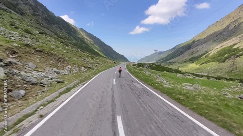 Epic shot of a cyclist conquering a mountain pass. Stunning landscape with clear blue skies and lush greenery. Perfect for travel, adventure, and sports themes. High-quality footage for your projects.