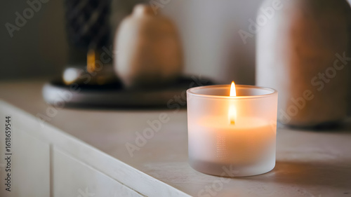 Lit candle in a frosted glass holder, placed on a contemporary dresser amid a cozy home interior.